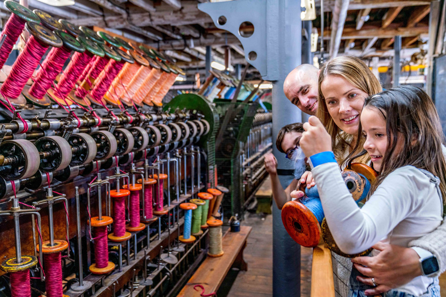 A young girl is with her family looking at an industrial threading machine.