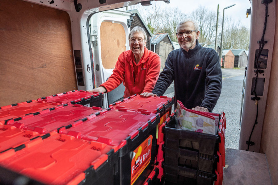 2 volunteers from Food Train organise food crates in the back of a van.