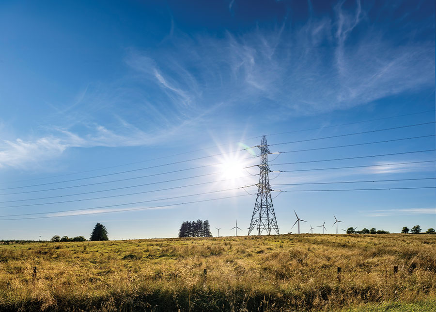 Sun beaming from behind pylon, with windfarm in background